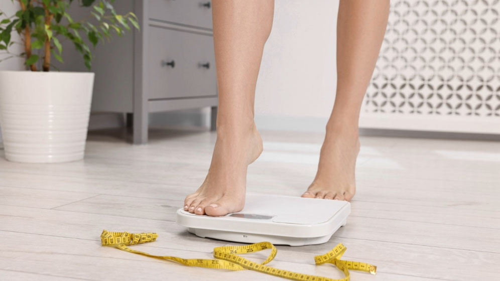 Close-up of woman stepping on a floor scale with measuring tape nearby.